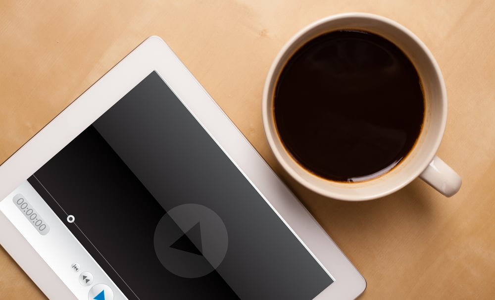 Workplace with tablet pc showing media player and a cup of coffee on a wooden work table close-up