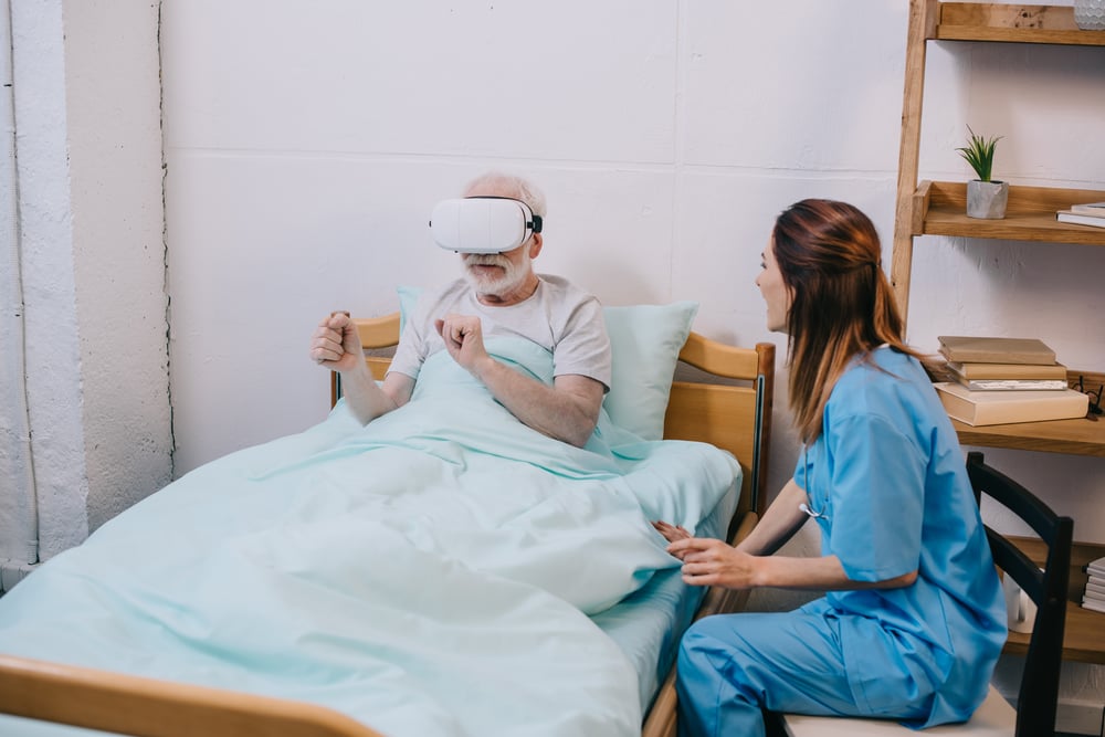 nurse-sitting-by-old-man-using-vr-glasses-6W4U6EY